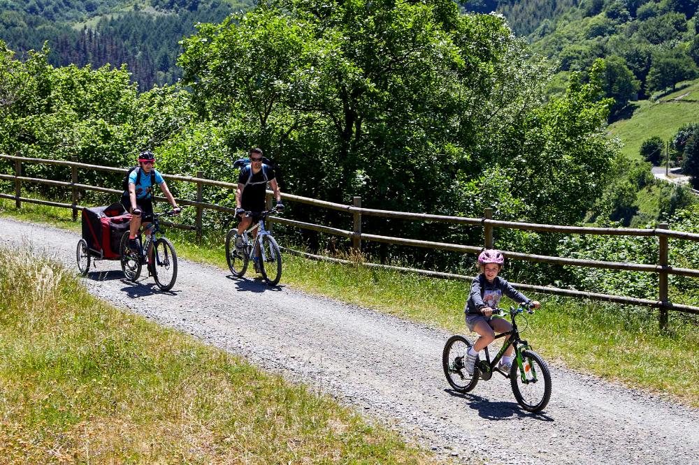 Dos adultos y un niño andando en bici por la vía verde del Plazaola